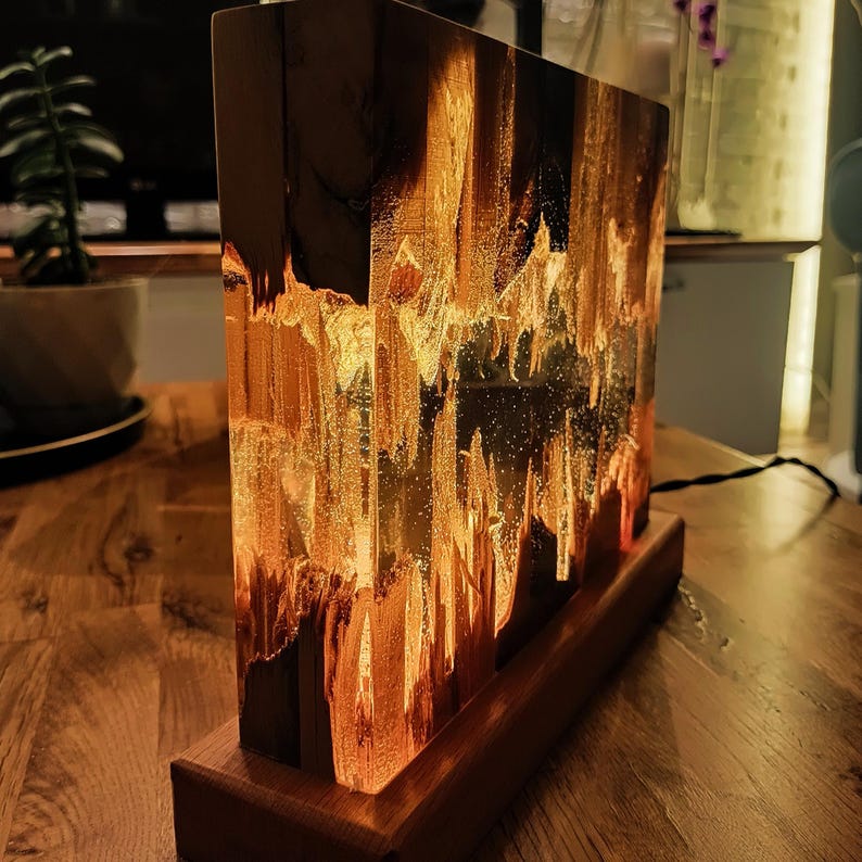 The Fission Resin Lamp, an Epoxy Resin Nightlamp with Oak Wood & Resin Decor, is a Wooden Modern Table Lamp ideal for home decor. This Resin Nightstand Lamp combines natural oak and epoxy resin, offering a sleek, contemporary glow for your nightstand or living space in a unique, handcrafted design.
