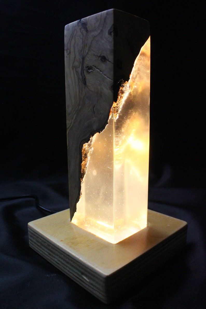 May include: A wooden and clear resin lamp with a warm, glowing light. The lamp has a natural wood base and a clear resin body with a wood grain pattern.