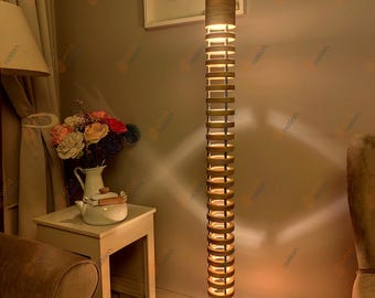 May include: A tall, wooden floor lamp with a cylindrical shade made of stacked rings. The lamp is lit and casting a warm glow on the surrounding room.