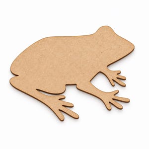 May include: A flat, light brown, laser-cut wooden cutout in the shape of a frog. The silhouette features a smooth, matte surface with a visible wood grain texture, depicting the frog in a seated profile position with four distinct webbed feet.