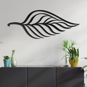 May include: Black metal leaf wall art with a modern design. The leaf is hanging on a white wall above a black dresser with three drawers. There are three potted plants on the dresser and a potted plant on a stand to the left of the dresser.