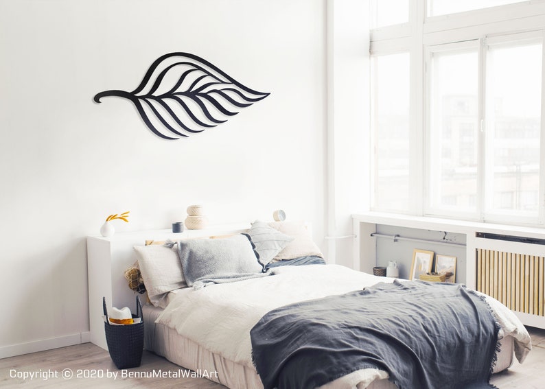 May include: Black metal leaf wall art hanging above a bed with white bedding and a gray throw blanket. The bedroom has a white wall and large windows.