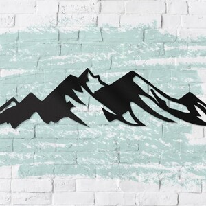 May include: Black metal silhouette of a mountain range against a white brick wall with a light blue painted background.
