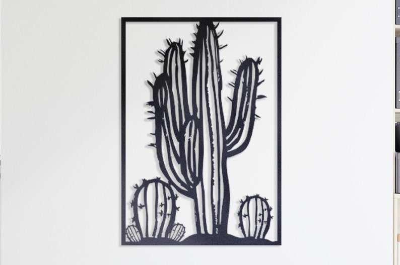 Puede incluir: Arte de pared de metal negro con la silueta de un cactus grande con dos cactus m&aacute;s peque&ntilde;os en primer plano. El arte est&aacute; enmarcado con un borde negro.