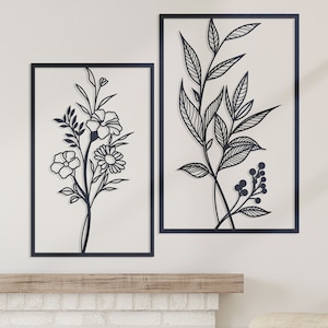 Może przedstawiać: Dwa czarne metalowe obrazy ścienne z kwiatowymi wzorami. Element po lewej stronie przedstawia bukiet kwiatów, a element po prawej stronie przedstawia gałąź z liśćmi i jagodami.