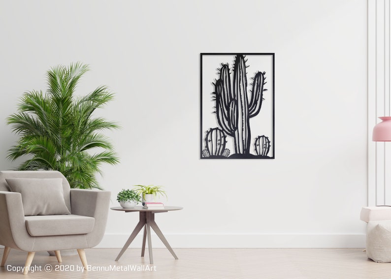 Puede incluir: Arte de pared de metal negro con una silueta de un cactus con un total de tres cactus. El arte est&aacute; enmarcado en un marco cuadrado negro y est&aacute; colgado en una pared blanca.
