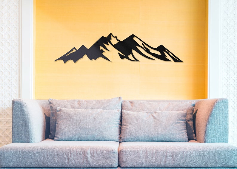 May include: A black metal mountain range wall decor silhouette mounted on a yellow wall above a light gray couch with two pillows.