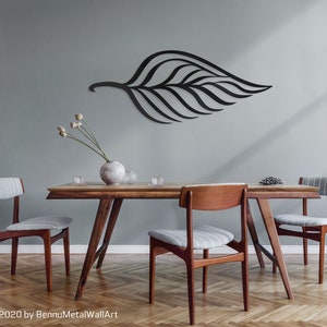 May include: A black metal leaf wall art sculpture hangs on a light gray wall above a wooden dining table with four chairs. The table has a light wood finish and the chairs have gray and white striped fabric seats.
