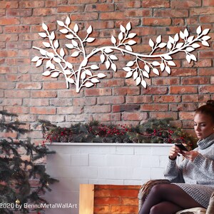 May include: White metal wall art in the shape of a leafy branch, mounted on a red brick wall. The artwork is a decorative element, adding a touch of nature to the interior. The image also includes a Christmas tree and a person.