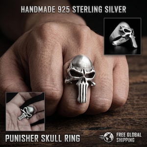 May include: A handmade 925 sterling silver Punisher skull ring. The ring features a detailed skull design with vertical lines below the jaw. The ring is shown on a hand, with additional images of the ring.