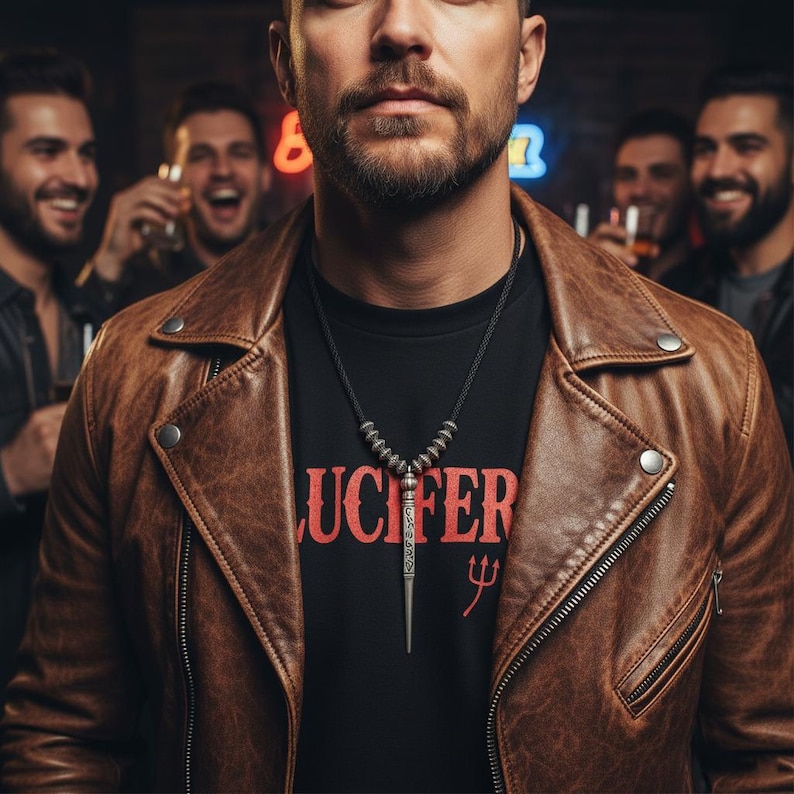Może przedstawiać: Brązowa sk&oacute;rzana kurtka na czarnym t-shircie ze słowem "LUCIFER" w kolorze czerwonym. Srebrny naszyjnik z wisiorkiem. Kilku mężczyzn w tle, niekt&oacute;rzy trzymają drinki.