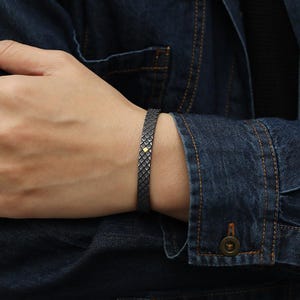 Puede incluir: Un brazalete negro con un patr&oacute;n geom&eacute;trico texturizado. El brazalete tiene un peque&ntilde;o acento dorado.