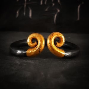 May include: A gold and black ring with a spiral design. The ring is made of two pieces, one gold and one black, that are joined together.