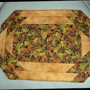 May include: A brown and green table runner with a leaf pattern and a brown suede border.