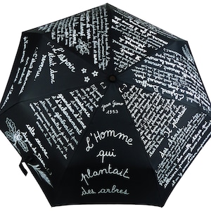 Peut inclure: Parapluie noir avec du texte blanc. Le texte dit "L'Homme qui plantait des arbres" et comprend une citation de Jean Giono, 1953. Le parapluie est recouvert de texte français.