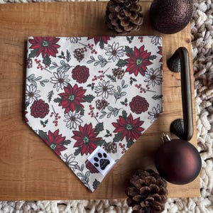 May include: A white bandana with a red and white floral pattern. The bandana has a white paw print logo in the bottom corner.