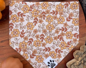 May include: A white bandana with a brown and yellow floral pattern. The bandana has a small white patch with a black paw print and the text "Love and Paw" on it.