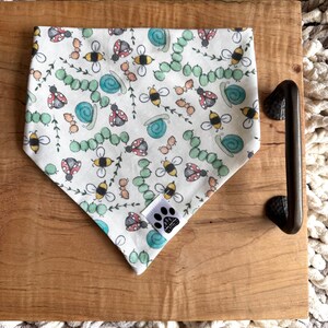 May include: White bandana with a pattern of ladybugs, bees, snails, and green leaves. The bandana has a small paw print logo in the bottom center.