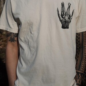 May include: A white t-shirt with a black and white graphic of a hand on the front.