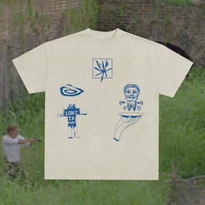 Pode incluir: Camiseta creme com desenhos gráficos azuis. A camiseta apresenta várias ilustrações, incluindo uma espiral, uma forma geométrica, uma figura segurando um prato e uma figura semelhante a um robô com o texto "LONE TA".