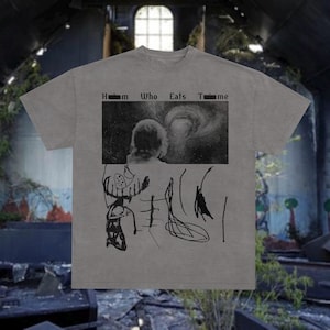 Könnte beinhalten: Graues T-Shirt mit einer schwarz-weißen Grafik. Die Grafik enthält den Text "Him Who Eats Time" über einem Schwarz-Weiß-Bild einer Person und eines Wirbelsturms. Darunter befinden sich abstrakte schwarze Zeichnungen.