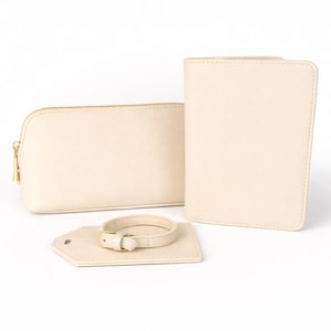 Beige Reise-Set aus Kosmetiktasche, Reisepasshülle und Kofferanhänger mit goldfarbenen Details auf hellem, neutralem Hintergrund