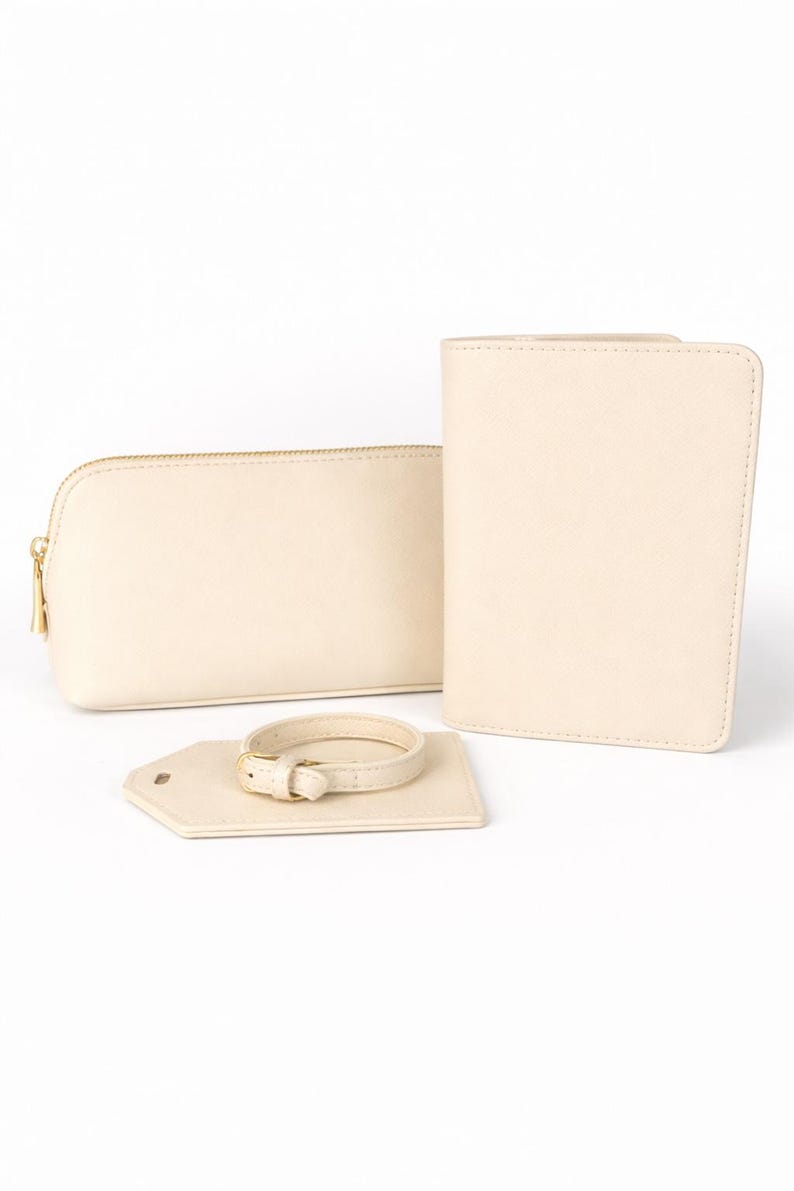 Beige Reise-Set aus Kosmetiktasche, Reisepasshülle und Kofferanhänger mit goldfarbenen Details auf hellem, neutralem Hintergrund