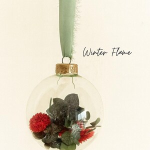 Personalisierte Weihnachtskugel aus Glas mit goldenem Kranz und grünen Chiffon-Aufhänger, gefüllt mit roten Phalaris-Trockenblumen und grünem Eukalyptus, Variante ‚Winter Flame‘.