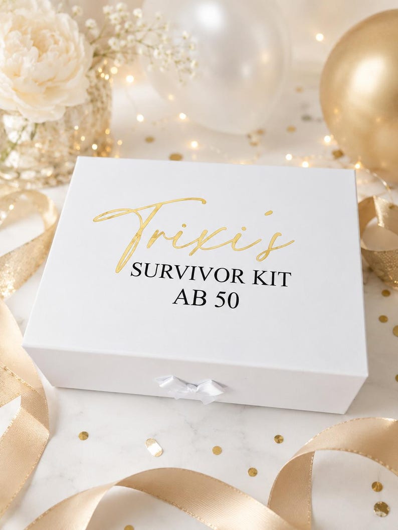 Weiße Geschenkbox mit goldener Aufschrift „Trixis Survivor Kit ab 50“ in feierlicher Dekoration mit goldenen Bändern, Konfetti, Blumen und Ballons auf hellem Hintergrund.