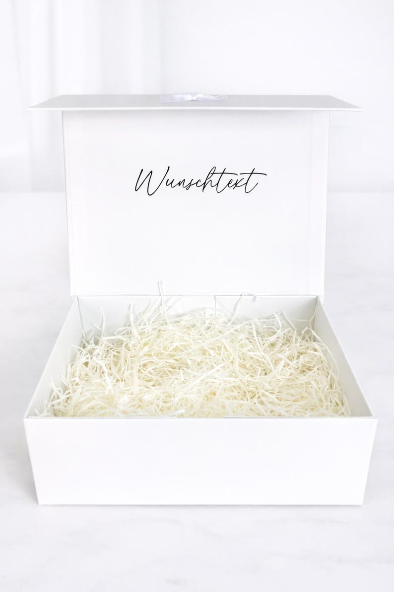 Weiße offene Geschenkbox mit neutralem Füllmaterial aus weißer Holzwolle, Innenseite mit Schriftzug „Wunschtext“, auf hellem Hintergrund.