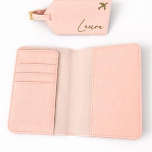 Personalisierte Reisepasshülle in Rosa mit Kartenfächern und passendem Kofferanhänger mit Name und Flugzeugsymbol auf hellem, neutralem Hintergrund