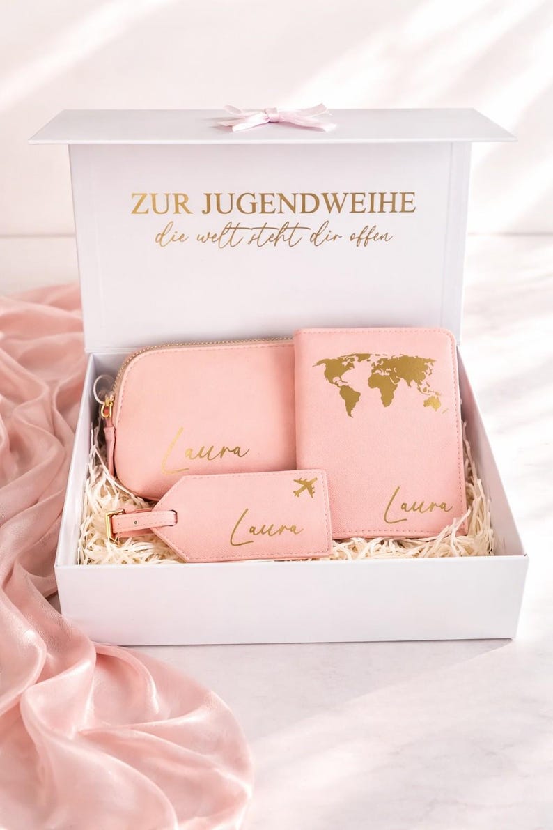 Personalisierte Geschenkbox zur Jugendweihe für Mädchen mit rosa Reiseset bestehend aus Kosmetiktasche, Reisepasshülle und Kofferanhänger in Goldschrift, stilvoll in weißer Box mit hellem Hintergrund und zartrosa Seidentuch inszeniert