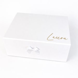 Personalisierte weiße Geschenkbox mit Name Laura in Goldschrift und kleiner Schleife auf hellem, neutralem Hintergrund