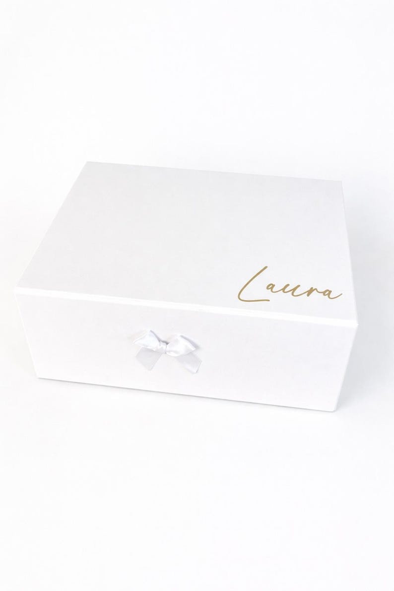 Personalisierte weiße Geschenkbox mit Name Laura in Goldschrift und kleiner Schleife auf hellem, neutralem Hintergrund