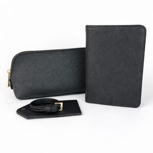 Schwarzes Reise-Set aus Kosmetiktasche, Reisepasshülle und Kofferanhänger aus strukturiertem Material mit goldfarbenem Reißverschluss auf hellem Hintergrund