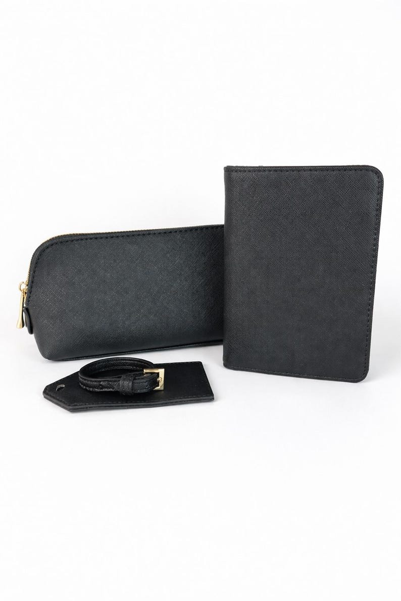 Schwarzes Reise-Set aus Kosmetiktasche, Reisepasshülle und Kofferanhänger aus strukturiertem Material mit goldfarbenem Reißverschluss auf hellem Hintergrund