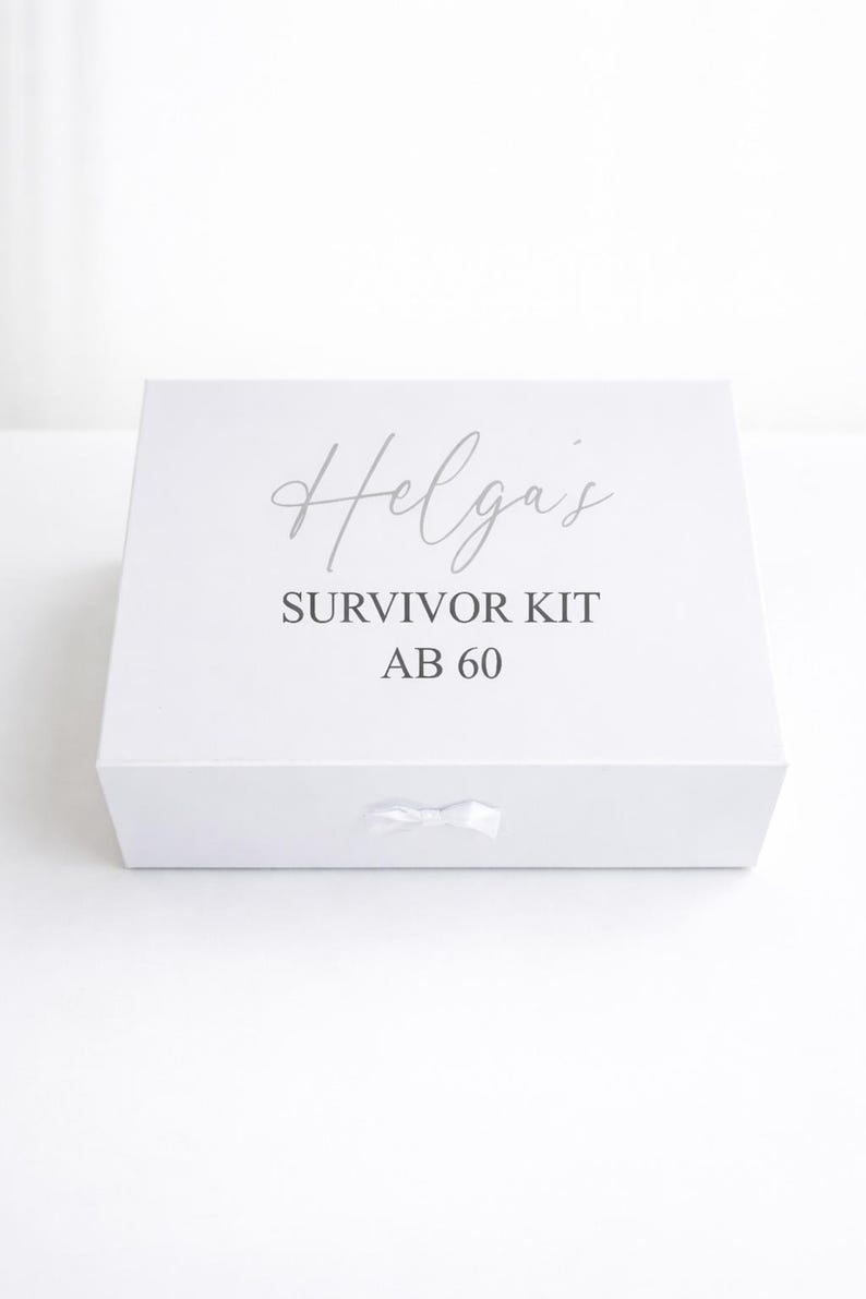 Weiße personalisierte Geschenkbox ‚Helga’s Survivor Kit ab 60‘ mit Schleife auf hellem, minimalistischem Hintergrund