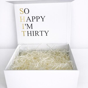 Offene weiße Geschenkbox zum 30. Geburtstag mit Schriftzug „SO HAPPY I’M THIRTY“ und Papierfüllung auf hellem Hintergrund