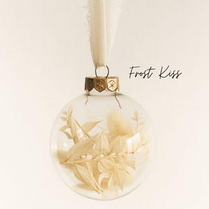 Personalisierte Weihnachtskugel aus Glas mit goldenem Kranz und weißen Chiffon-Aufhänger, gefüllt mit weißen Trockenblumen Lagurus und Ruscus, Variante ‚Frost Kiss‘.