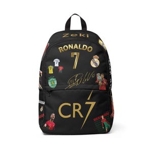 Könnte beinhalten: Ein schwarzer Rucksack mit goldenem Text, der Zeki, Ronaldo und CR7 lautet. Die Tasche zeigt verschiedene Bilder von Cristiano Ronaldo in Fußballtrikots, die Nummer 7, eine goldene Unterschrift, das Sporting CP-Logo und den Text SIUUUUU in Rot und Weiß.