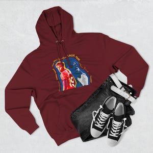 Könnte beinhalten: Burgunderfarbener Kapuzenpullover mit einer Grafik eines Fußballspielers, "Lamine Yamal". Das Bild zeigt eine dunkelblaue Jeans, einen weißen Gürtel und schwarz-weiße Turnschuhe. Auf dem Trikot des Spielers ist die Nummer 19 zu sehen.