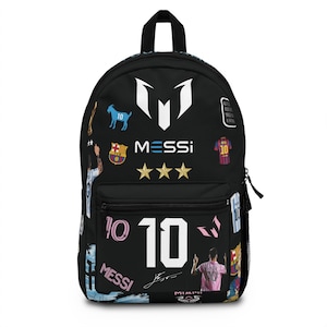Peut inclure: Un sac à dos noir orné de divers graphismes sur le thème de Lionel Messi, incluant le numéro 10, le logo Messi, trois étoiles dorées, une silhouette de chèvre bleue et des images de maillots de football. Le design inclut le texte Messi et une signature.