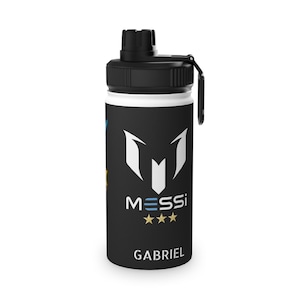 May include: A white water bottle with a black lid and handle. The bottle features a black section with the word "MESSI" and three stars, along with the name "GABRIEL". The bottle has a blue and yellow design on the side.