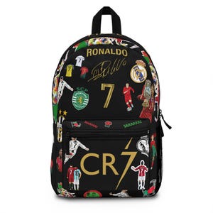 May include: Black backpack featuring a collage of soccer imagery, including the number 7, the name "RONALDO", and the initials "CR7". The backpack has a top handle, a front pocket, and a zipper closure.