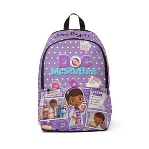 May include: A purple backpack with white polka dots featuring the Doc McStuffins logo, a butterfly, and the name Joslyn. The front pocket displays various cartoon characters, a checklist, and the text Caring makes everything better and Big Heart.