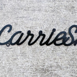 May include: Black metal sign with the text "The Carrie Shack" in a cursive font.
