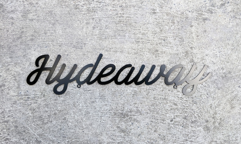 May include: Black metal sign with the word "Hydeaway" written in a cursive font.