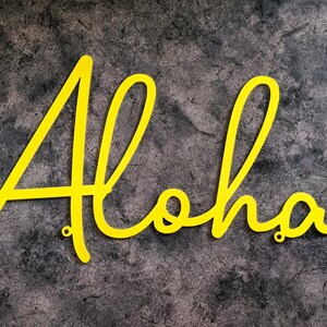 May include: Yellow metal letters spelling out the word "Aloha" on a gray textured background.