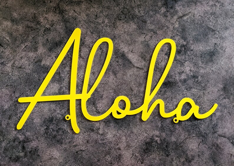 May include: Yellow metal letters spelling out the word "Aloha" on a gray textured background.