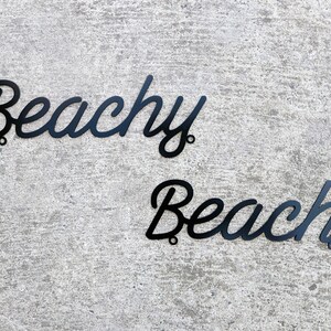 May include: Black metal wall decor with the words "Beachy Beach" in a cursive font.